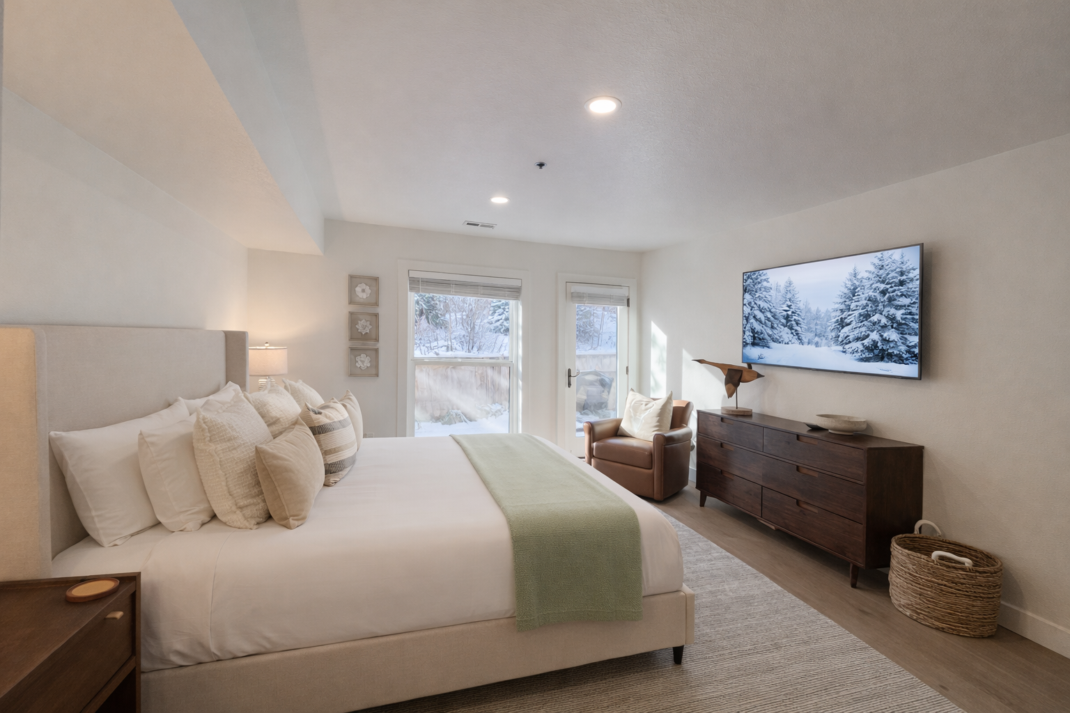 Relax in this bright, inviting bedroom with a plush king bed, crisp white linens, and a soft green throw. Large windows, cozy seating, and a TV with snowy mountain views create a perfect Park City retreat.