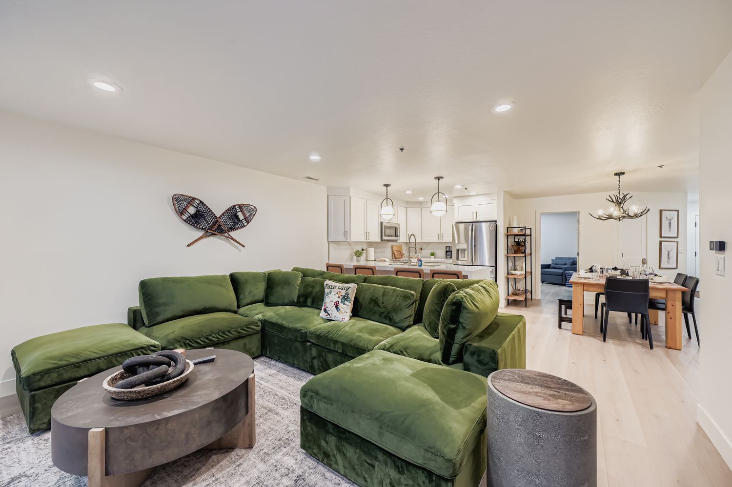Relax in your spacious open-concept living area featuring a plush emerald green sectional sofa, modern furnishings, and seamless flow to the fully-equipped kitchen.