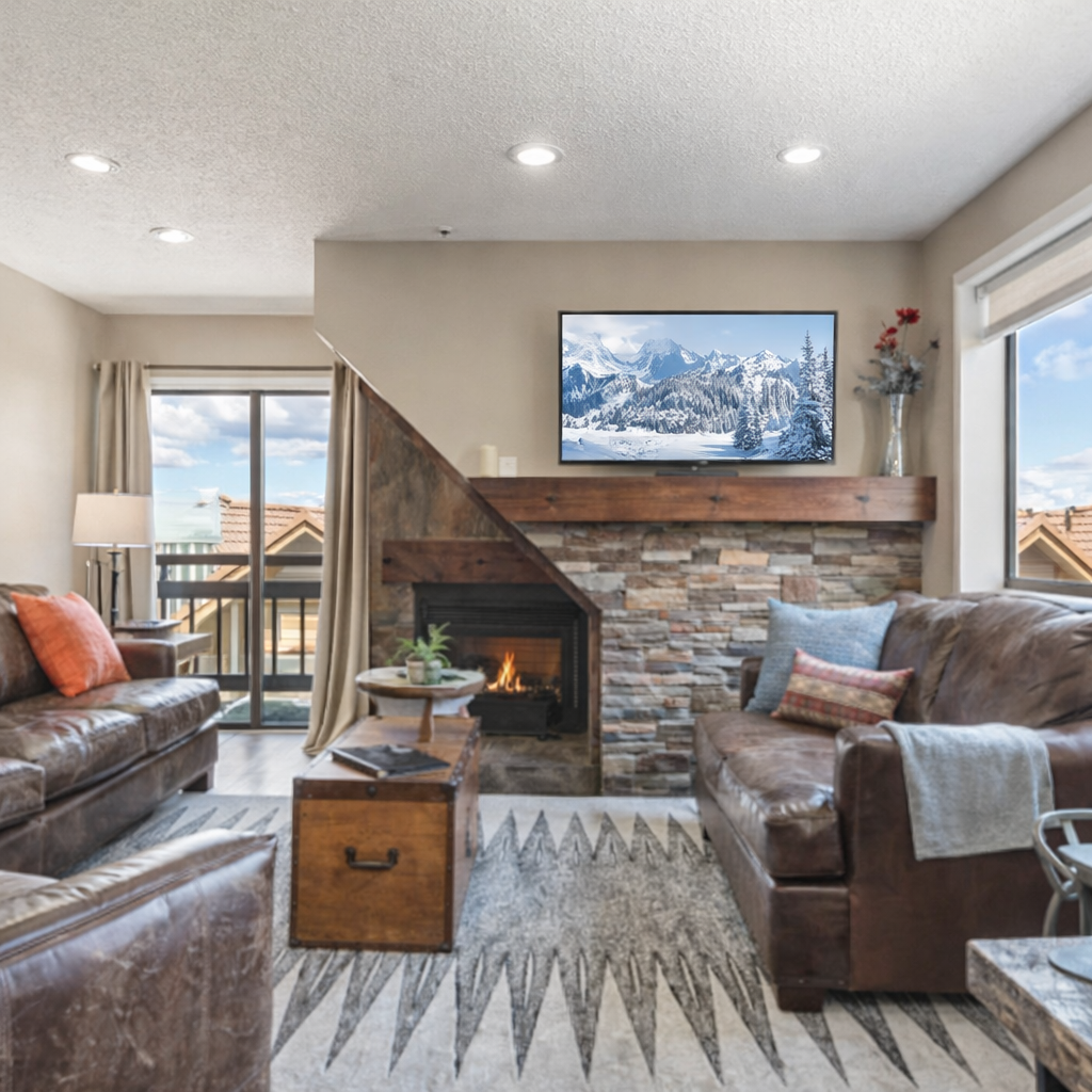 Bright mountain-style living room with stone fireplace, cozy leather seating, and smart TV. Open layout, natural light, and warm alpine décor create the perfect retreat after skiing or exploring Park City.