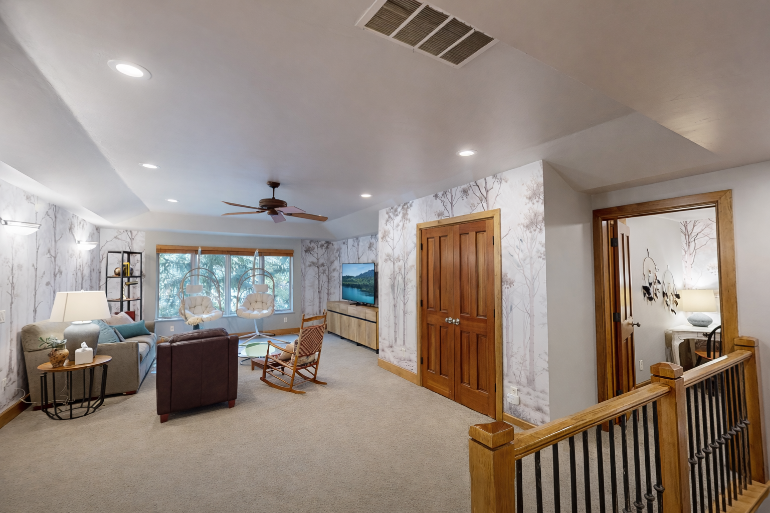 Unwind in your stylish living room with a unique hanging chair, cozy seating, and peaceful forest views through large windows.