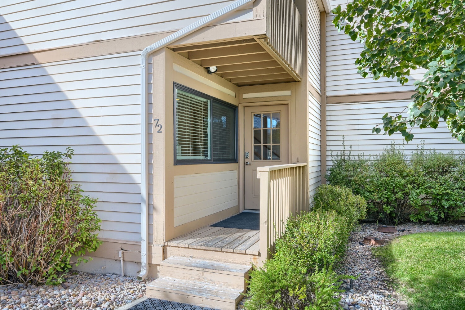 Unit 72 features a covered entrance with a welcoming porch and well-maintained landscaping, framed by mature greenery and a tidy lawn.