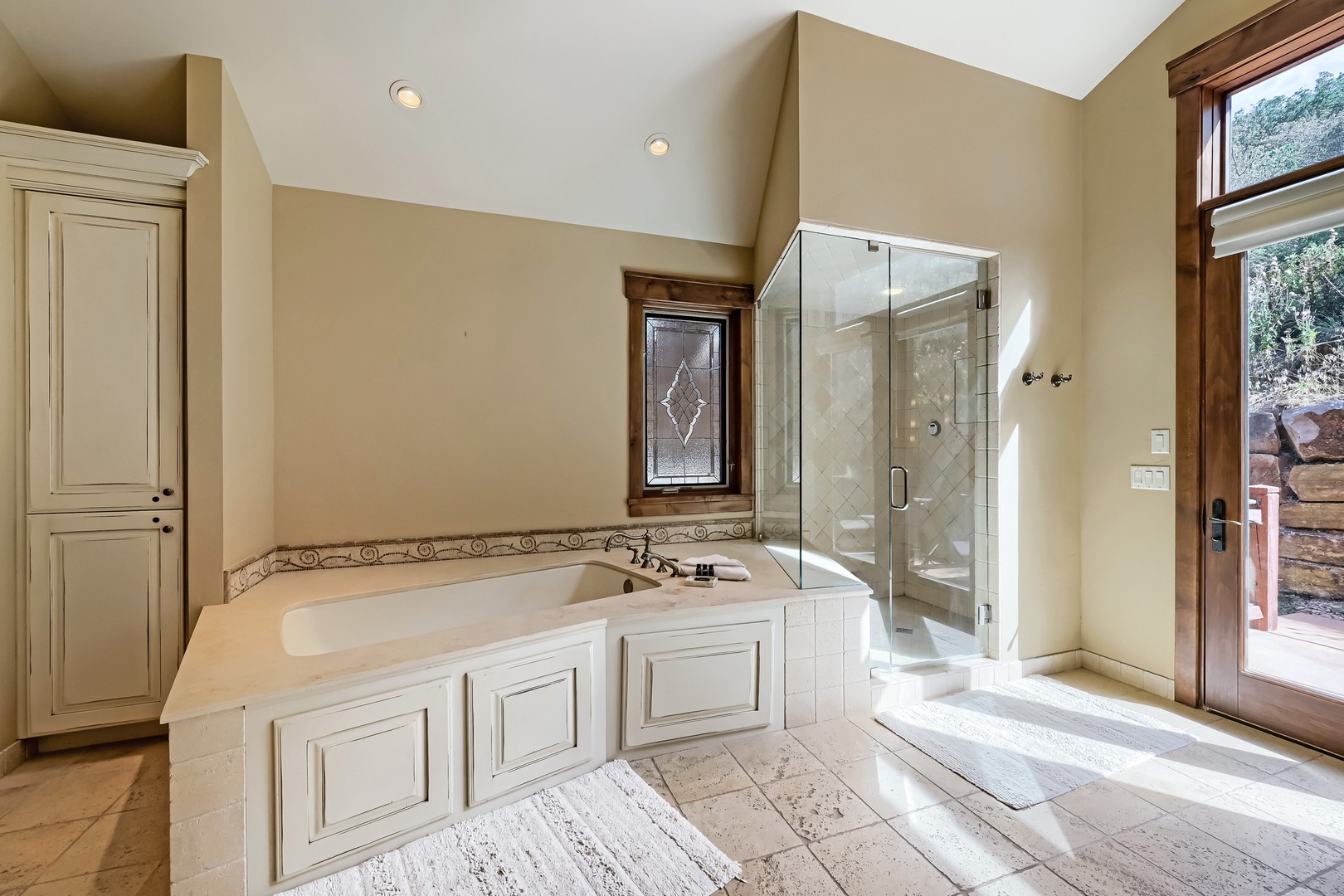 Private spa-like retreat with soaking tub and spacious glass-enclosed shower. Natural light illuminates the vaulted ceiling and elegant tilework, creating a peaceful sanctuary to unwind.