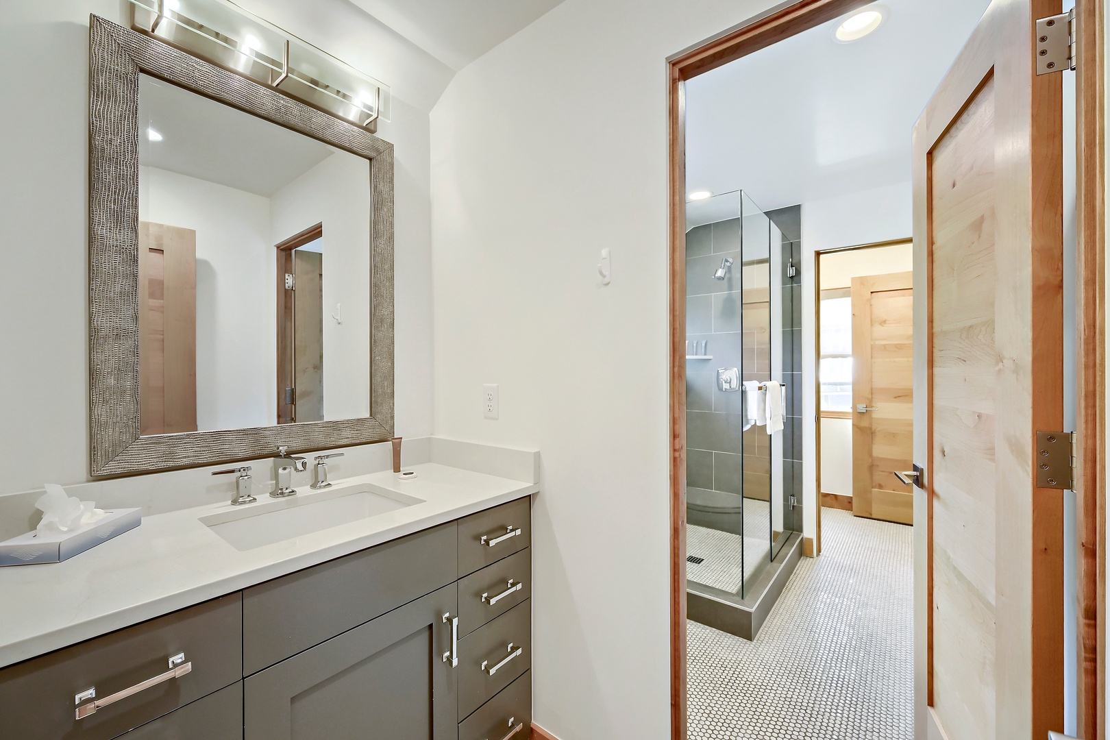 Your private en-suite bathroom offers a sleek vanity with fresh towels, elegant fixtures, and a spacious walk-in shower framed by warm wood accents—a serene spot to refresh and unwind.