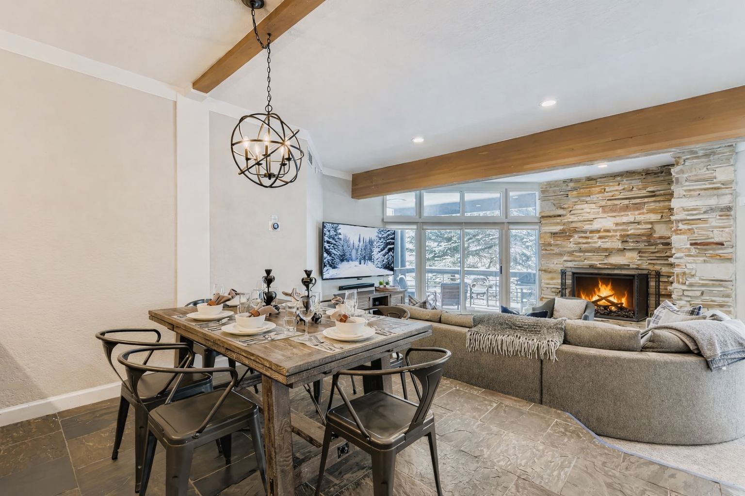 Relax in your open-concept living space featuring exposed wood beams, a cozy stone fireplace, and elegant dining area perfect for memorable meals together.