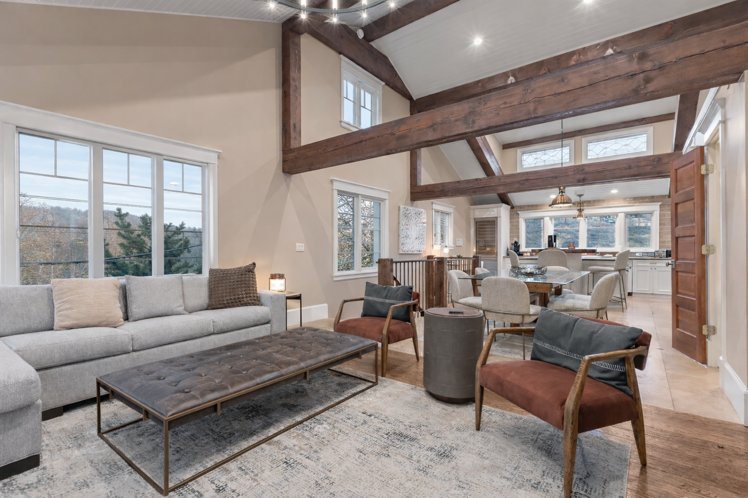 Unwind in your spacious open-concept living room featuring soaring ceilings with exposed beams and abundant natural light from panoramic windows.