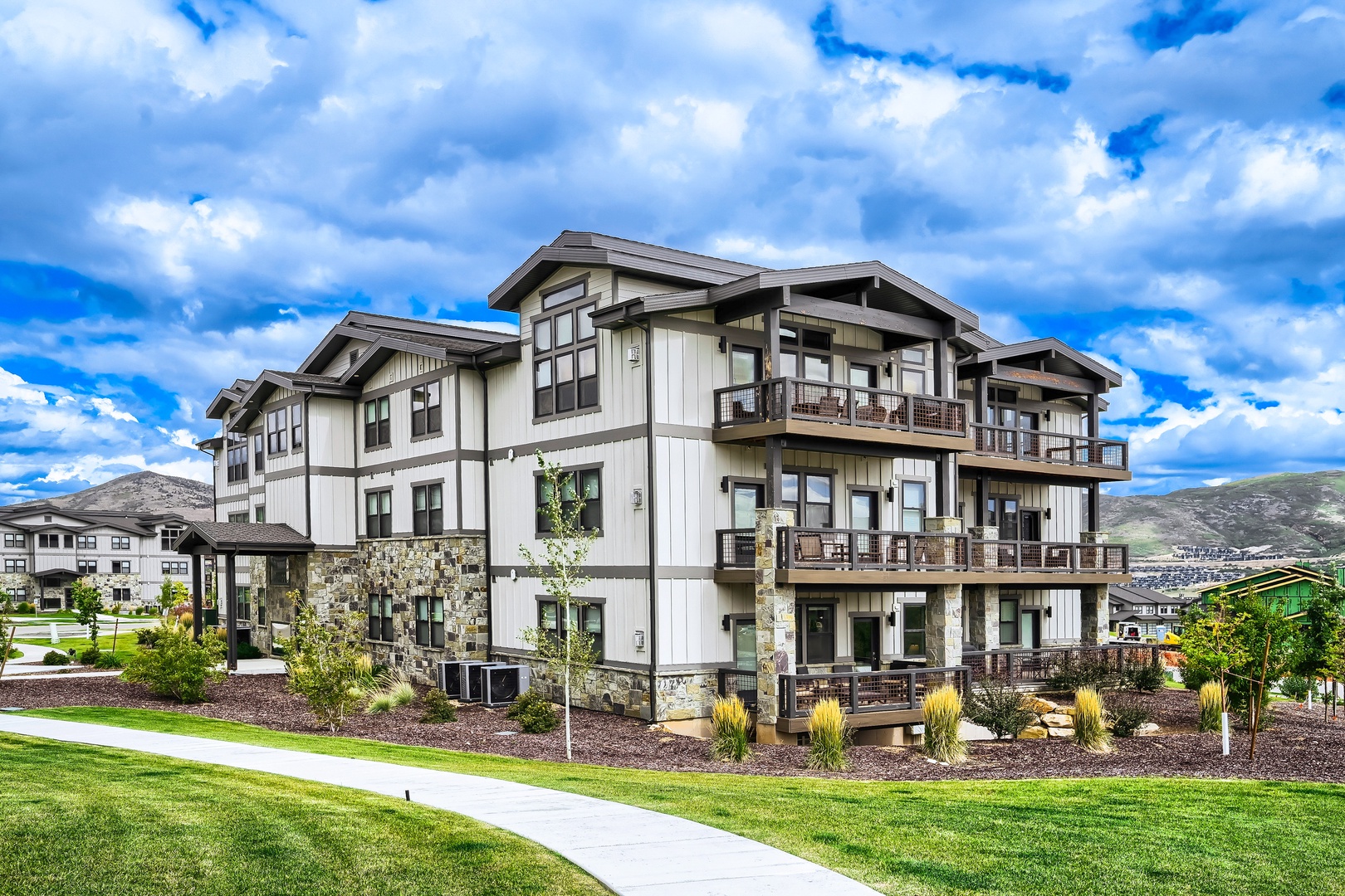 Modern mountain retreat with alpine architecture, spacious balconies, and manicured landscaping set against dramatic blue skies and rolling hillsides.