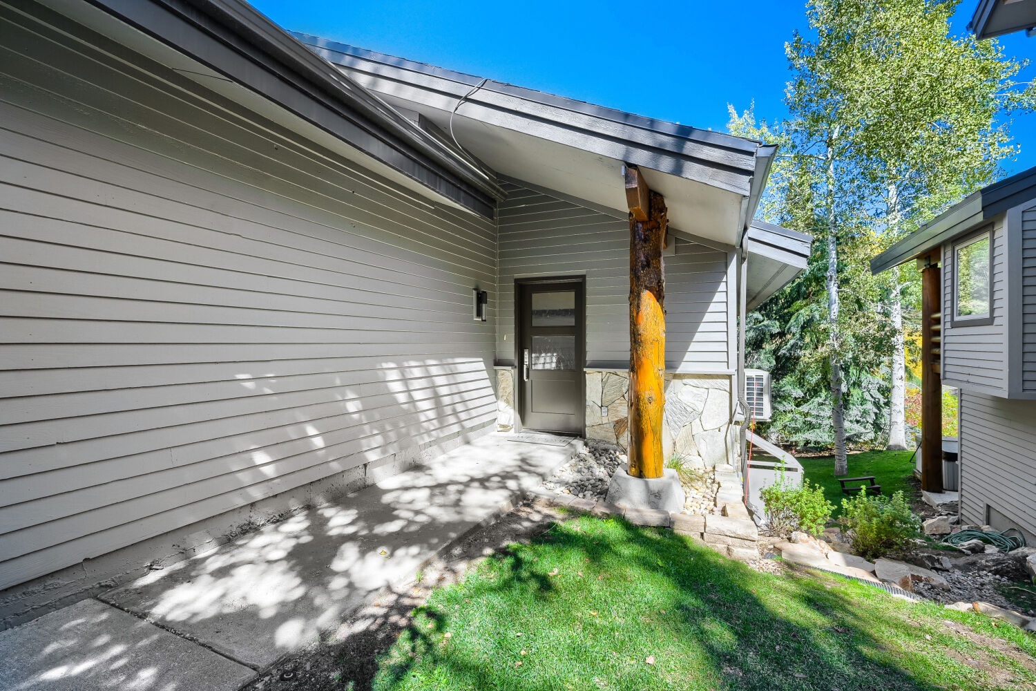 The property entrance, framed by mature trees and a natural wood column, offers a peaceful arrival experience with nearby greenery and mountain surroundings.