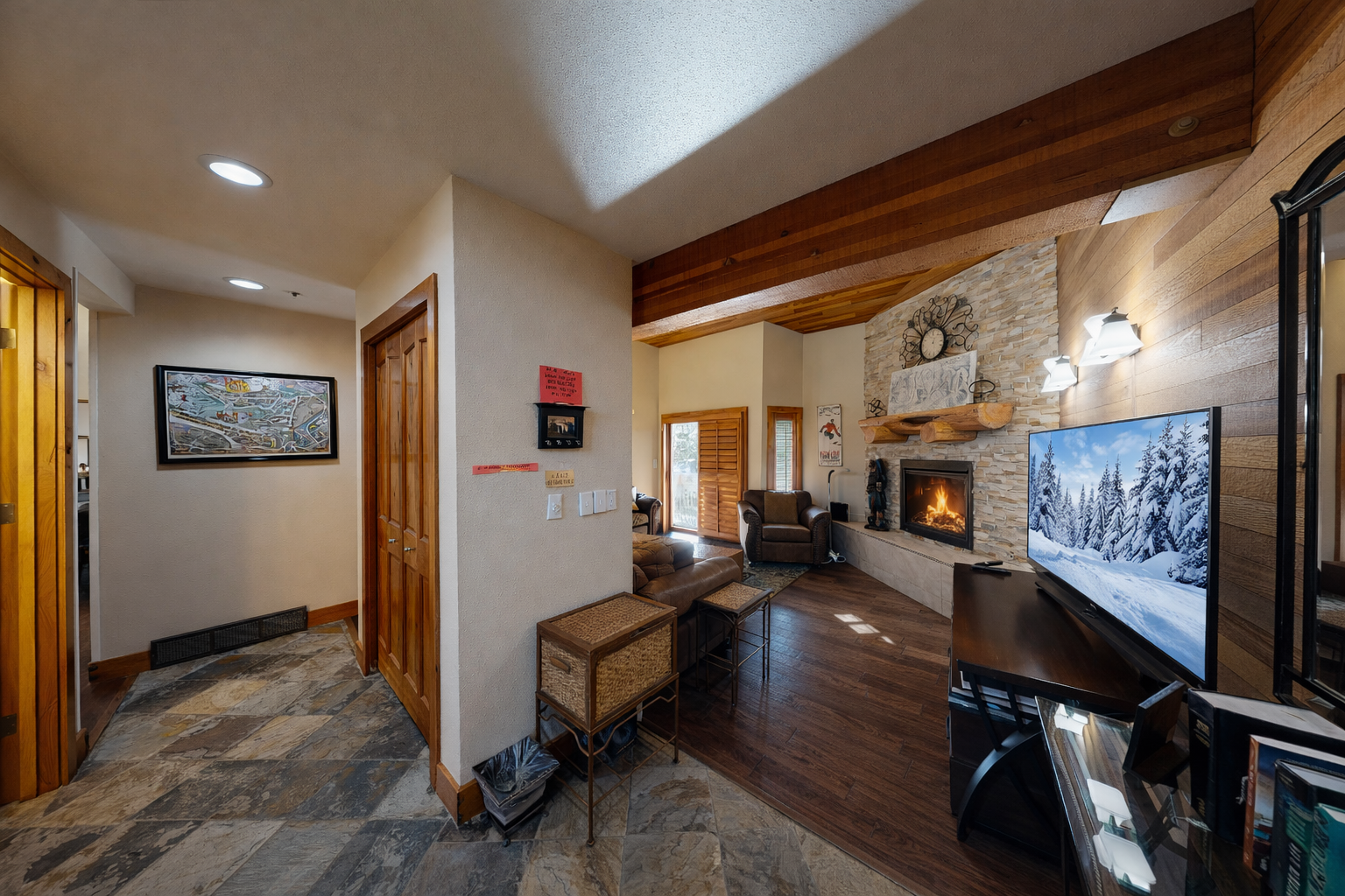 Cozy up in your spacious living room featuring exposed wooden beams, stone fireplace, and modern TV for perfect mountain evenings.