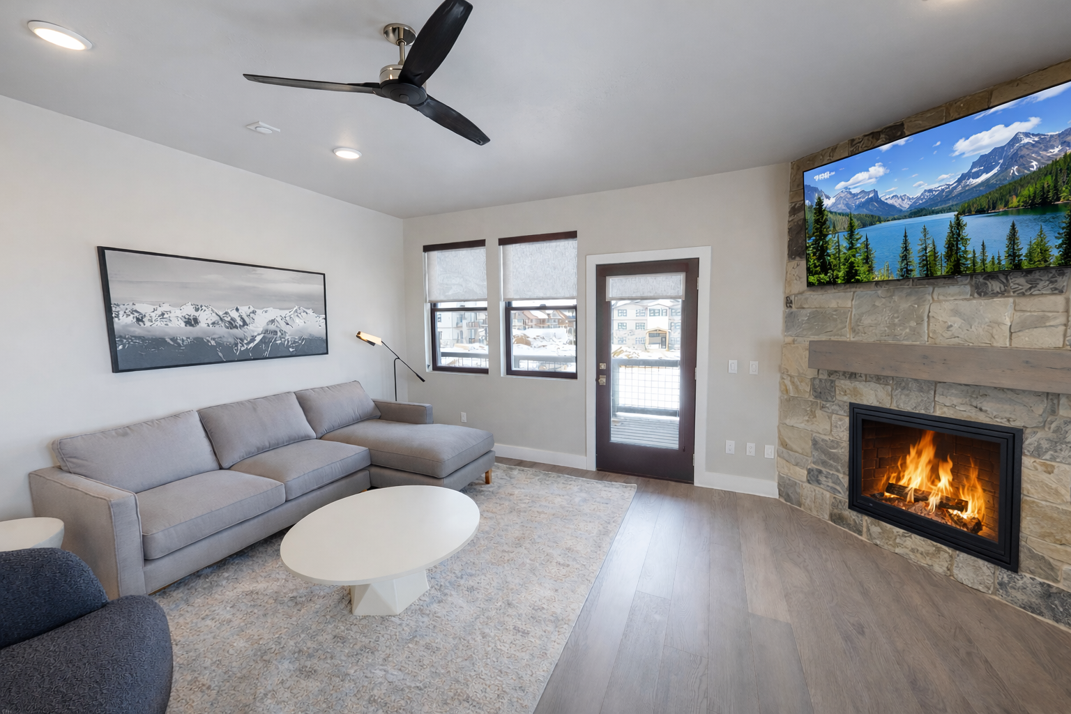 Relax in this airy, modern living room featuring a cozy stone fireplace and large windows with mountain views. The open layout and stylish furnishings make it the perfect spot for relaxing.