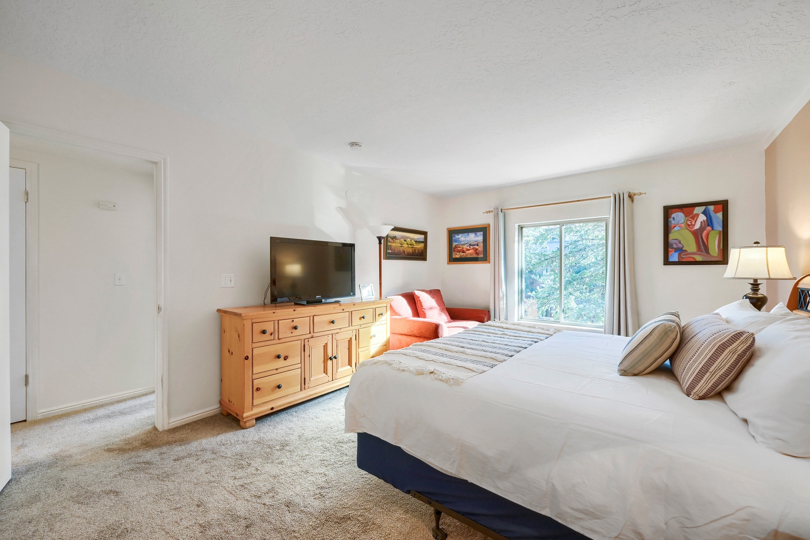 Sink into the plush king bed after a day exploring, with bright windows framing leafy views and a cozy reading chair waiting nearby.