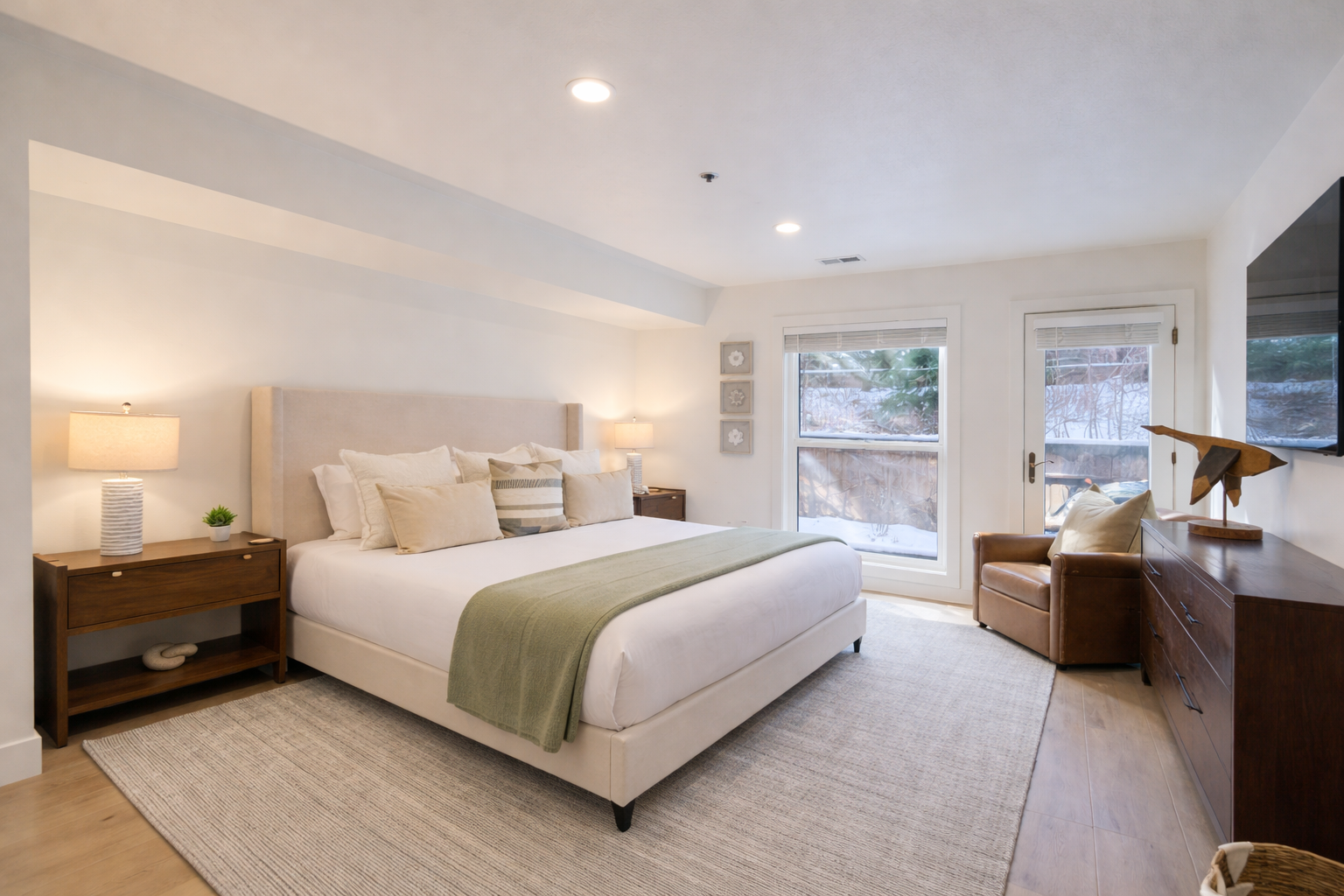 Bright, modern bedroom with a plush king bed, crisp white linens, and a soothing light-green accent throw. Enjoy large windows, cozy seating, and a calm, airy design—perfect for relaxing after a day exploring Park City.