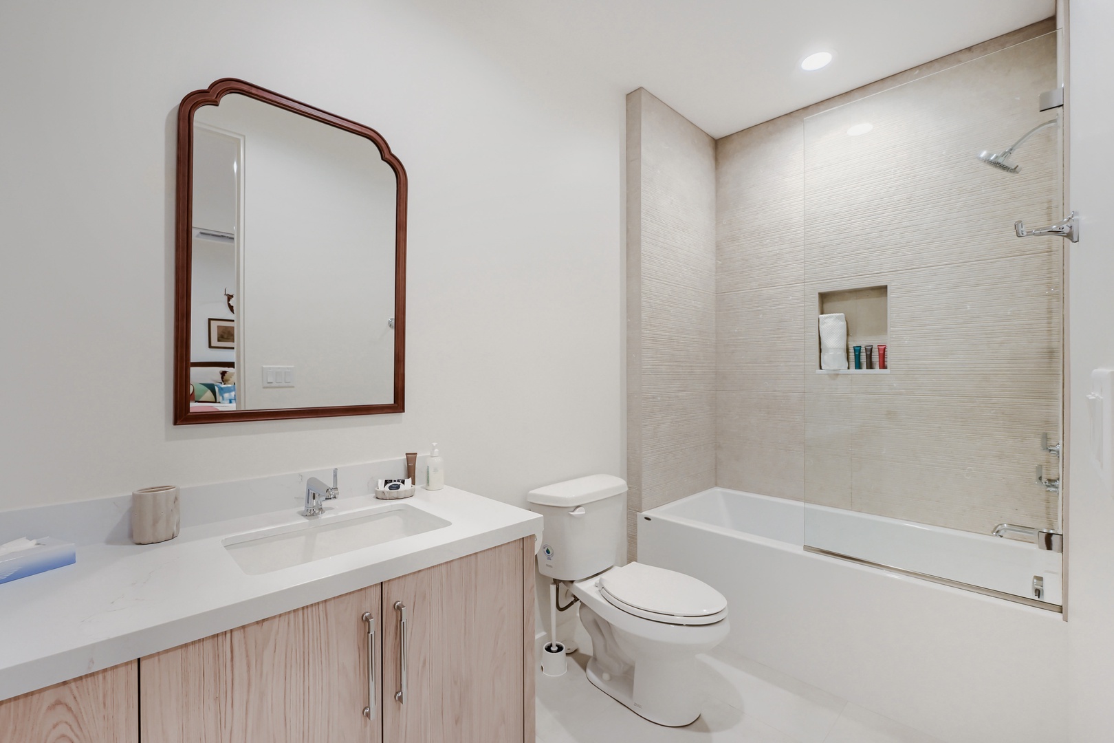 Step into your immaculately designed bathroom, where clean lines and soft textures meet. Warm wood tones beneath a gleaming white countertop frame your vanity, while the glass-enclosed tub awaits your relaxation after a day of adventure.