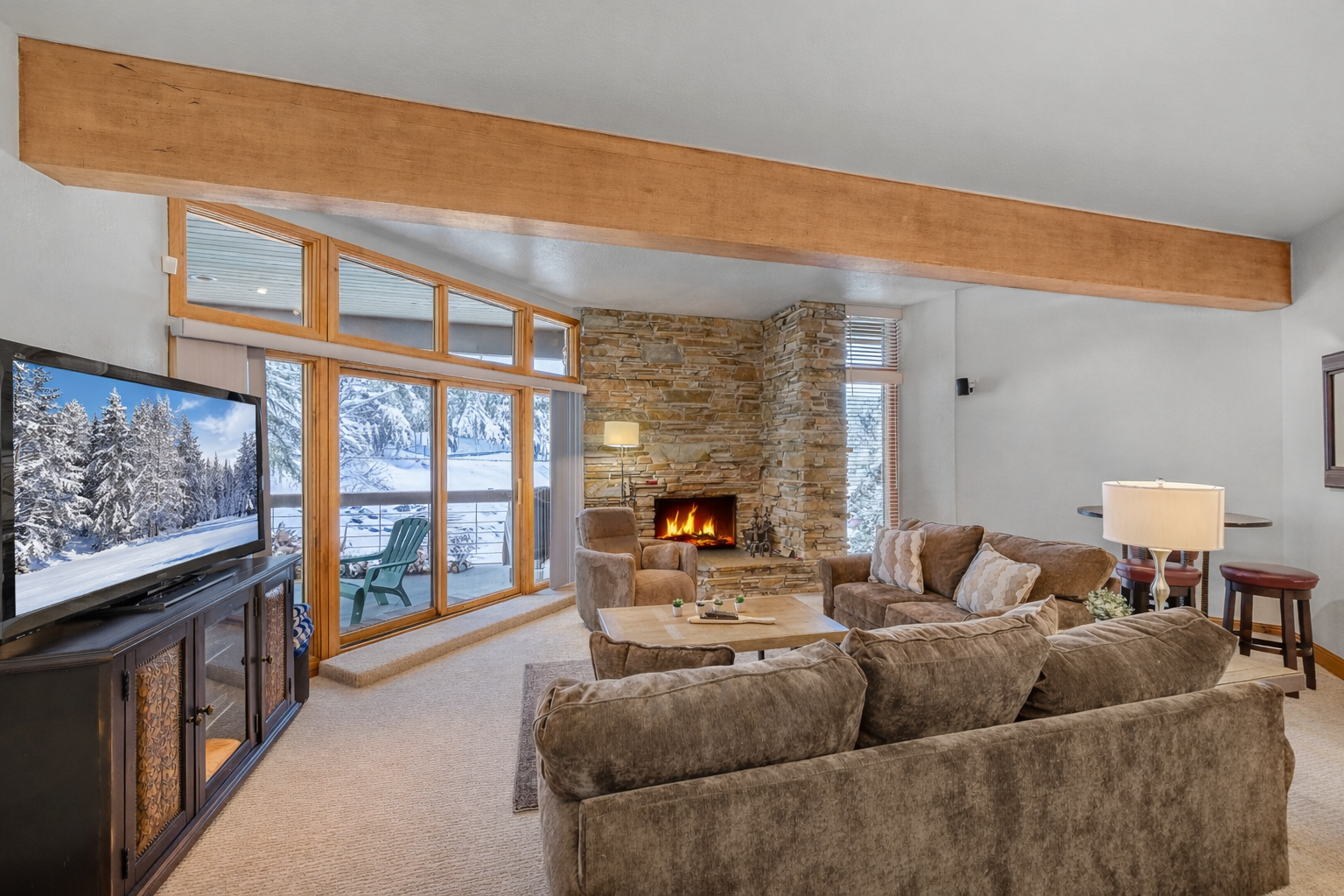 Curl up in your cozy living room with crackling fireplace, plush seating, and stunning winter mountain views through floor-to-ceiling windows.