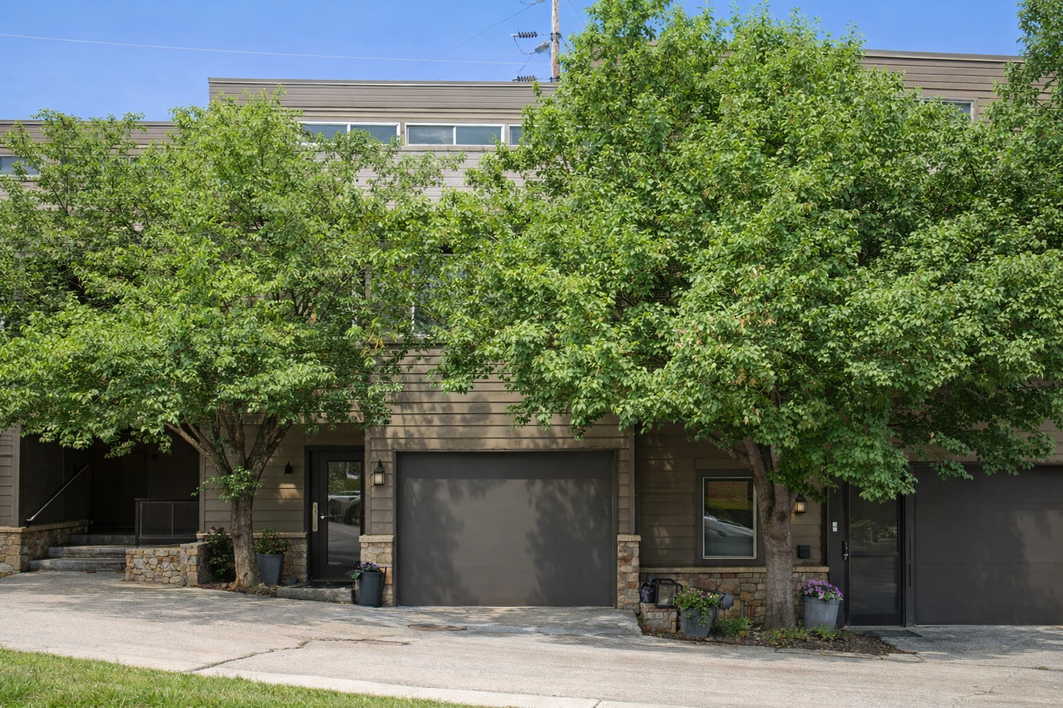 Modern property exterior featuring natural wood siding and mature shade trees in quiet residential neighborhood.