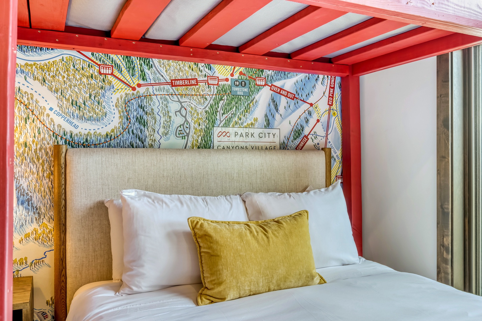 Unwind in your cozy sleeping nook featuring a plush bed, vibrant overhead canopy, and a custom local map headboard that connects you to the surrounding mountain adventure.