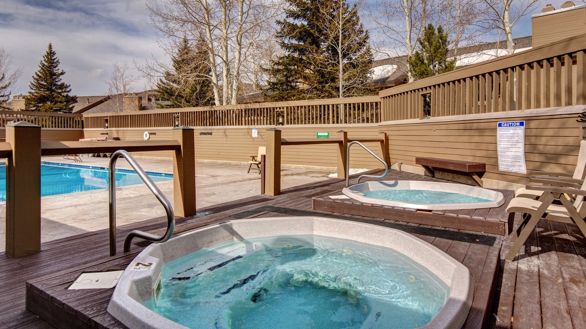Two inviting hot tubs on a wooden deck await you, offering the perfect spot to soak and unwind while surrounded by trees and mountain air.