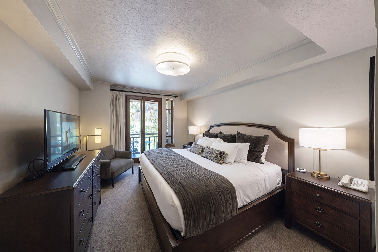 This spacious bedroom features a plush king-size bed with an elegant dark wood frame. Sliding glass doors open to a private balcony, offering stunning mountain views and plenty of natural light.