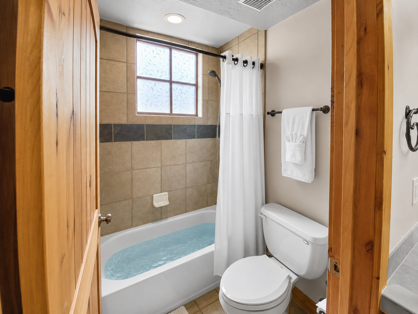 Spacious full bathroom featuring a large double vanity, ample storage in rustic wood cabinets, and a walk-in shower/tub combo with tiled walls. A clean and functional space for your stay.