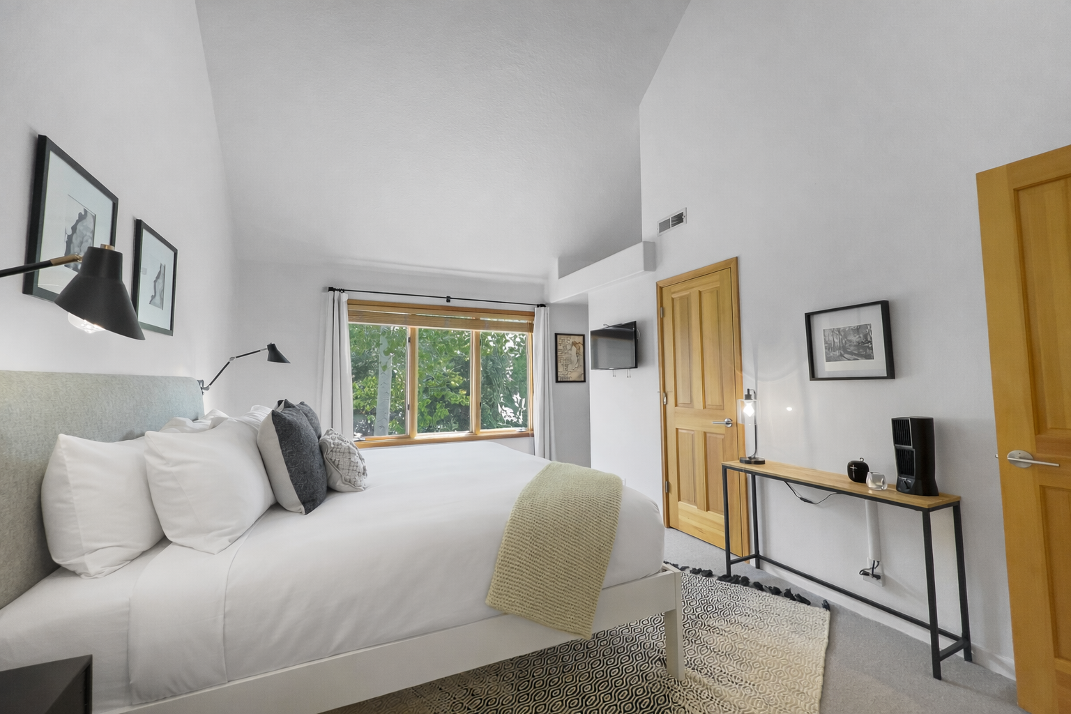 Retreat to this tranquil bedroom featuring a plush king-sized bed, a bright vaulted ceiling, and views of lush greenery for a serene escape.