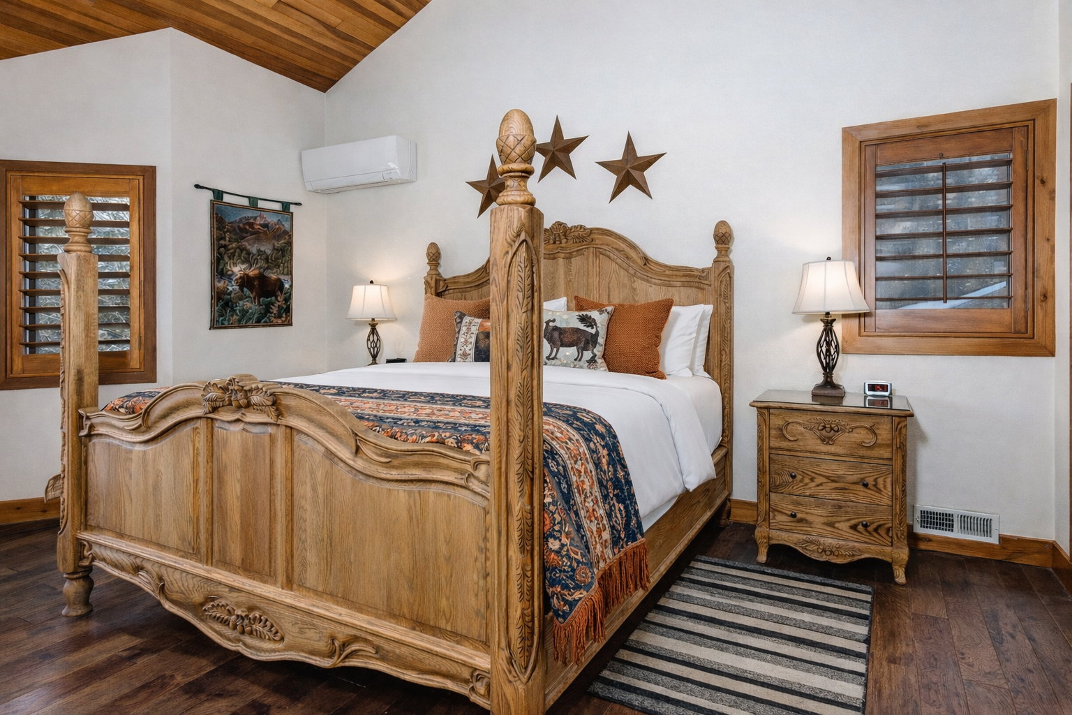 Relax in your spacious master bedroom featuring stunning wood beam ceilings, rustic furnishings, and modern amenities like AC and TV for the perfect mountain retreat.