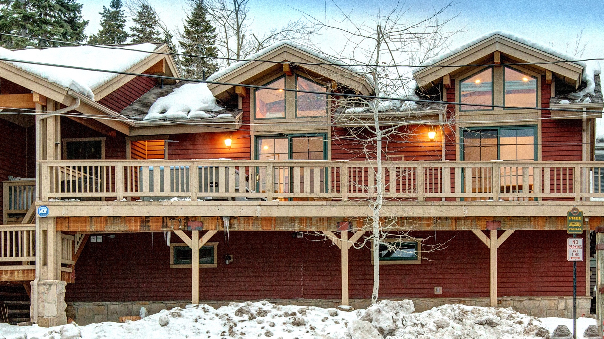 Multi-level wooden lodge nestled among snow-covered evergreens, featuring warm exterior lighting and spacious covered balconies perfect for winter mountain retreats.