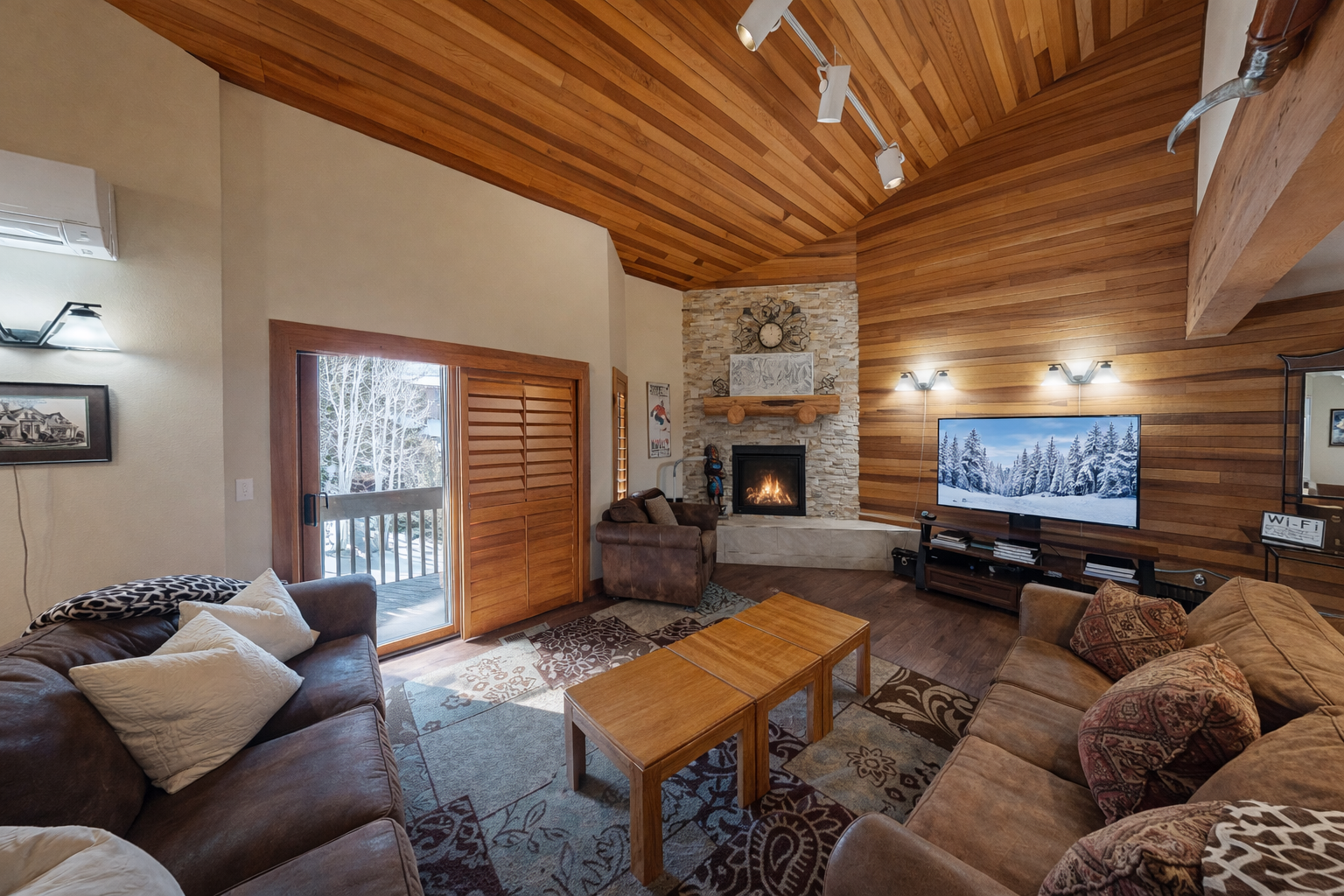 Unwind in this cozy, wood-paneled living room. Enjoy the warmth of the stone fireplace or step outside onto the snowy deck for fresh mountain air.