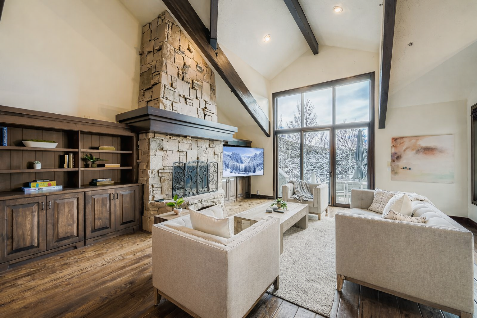Unwind in your elegant living room with soaring ceilings, stone fireplace, and serene winter views through expansive windows.