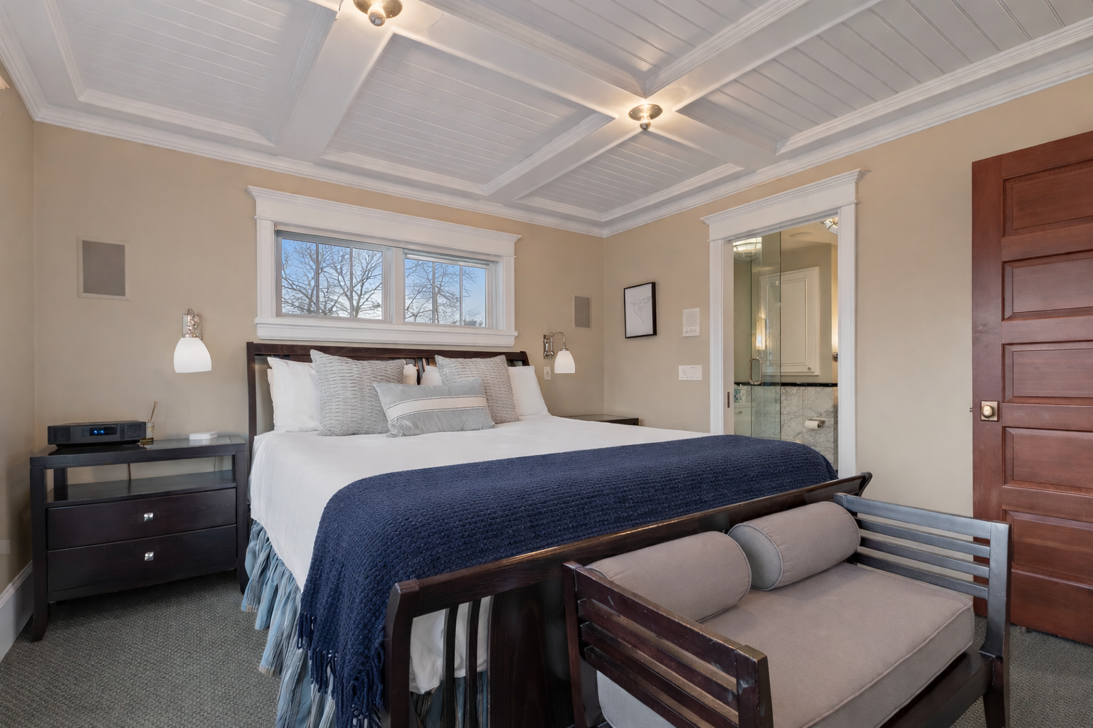 Relax in your elegant bedroom featuring crisp linens, a cozy navy throw, and beautiful coffered ceiling details.