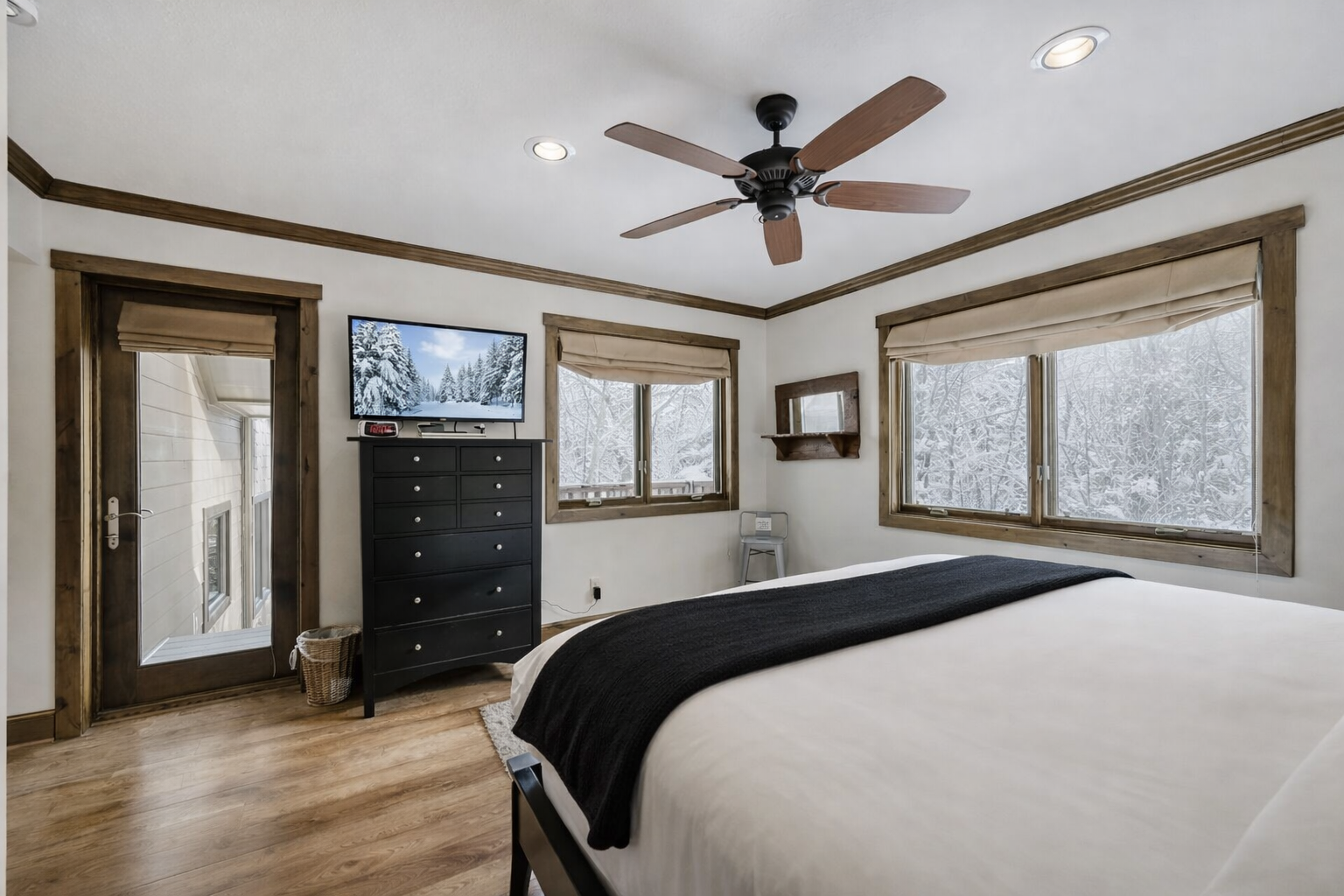 Your cozy bedroom features stunning winter mountain views through large windows, plus a flat-screen TV and ceiling fan for comfort.