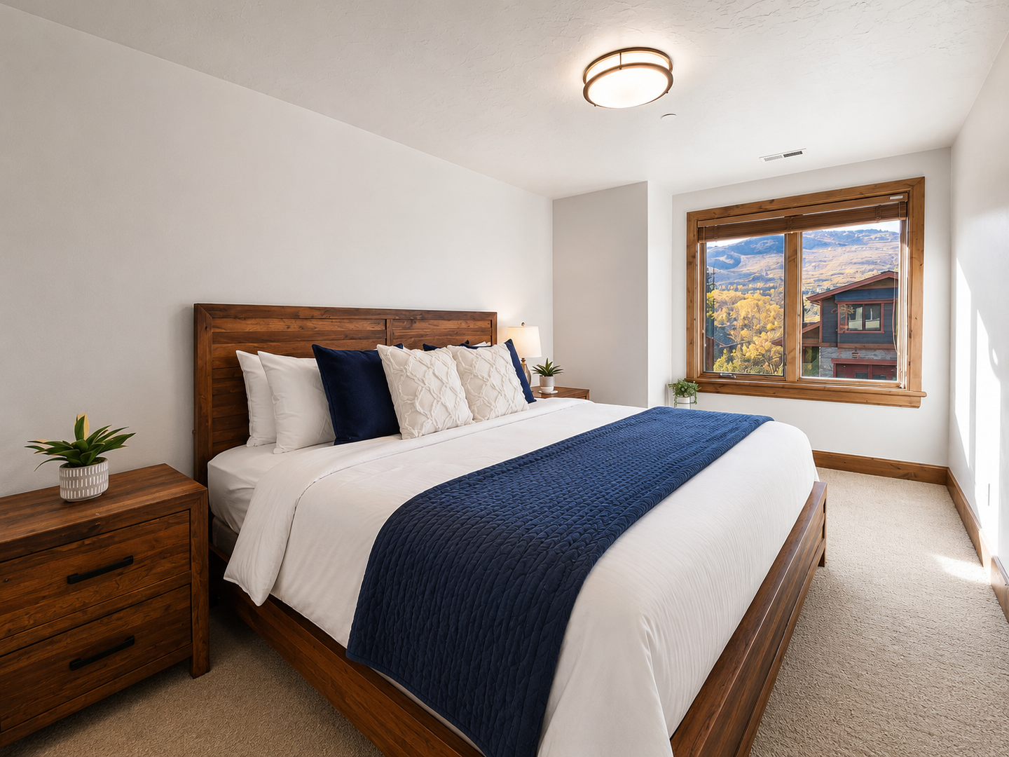This serene guest bedroom features a plush king bed with crisp linens and a stylish blue throw. Large wood-trimmed windows offer stunning mountain views from your pillow.