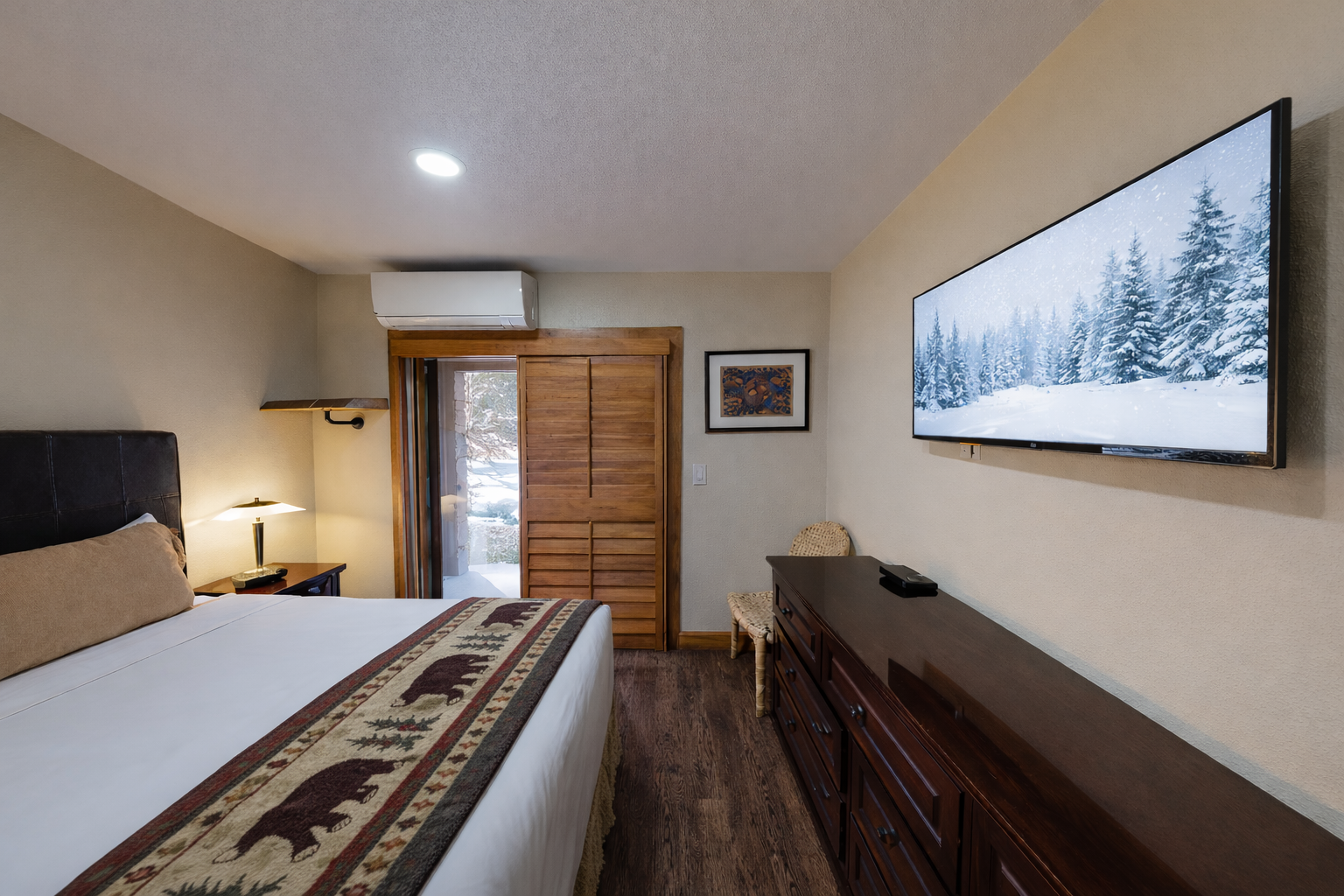 Unwind in your cozy bedroom with plush bedding, rustic wood touches, and a large TV for peaceful evenings after mountain adventures.