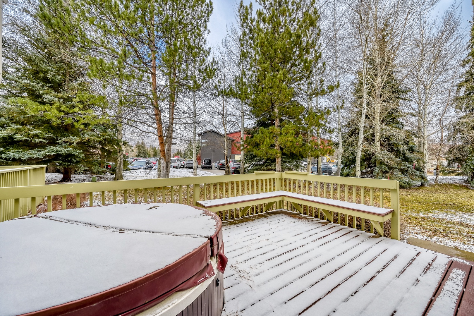 This property features a private deck with hot tub and built-in seating, surrounded by mature pines and evergreens in a peaceful residential setting.