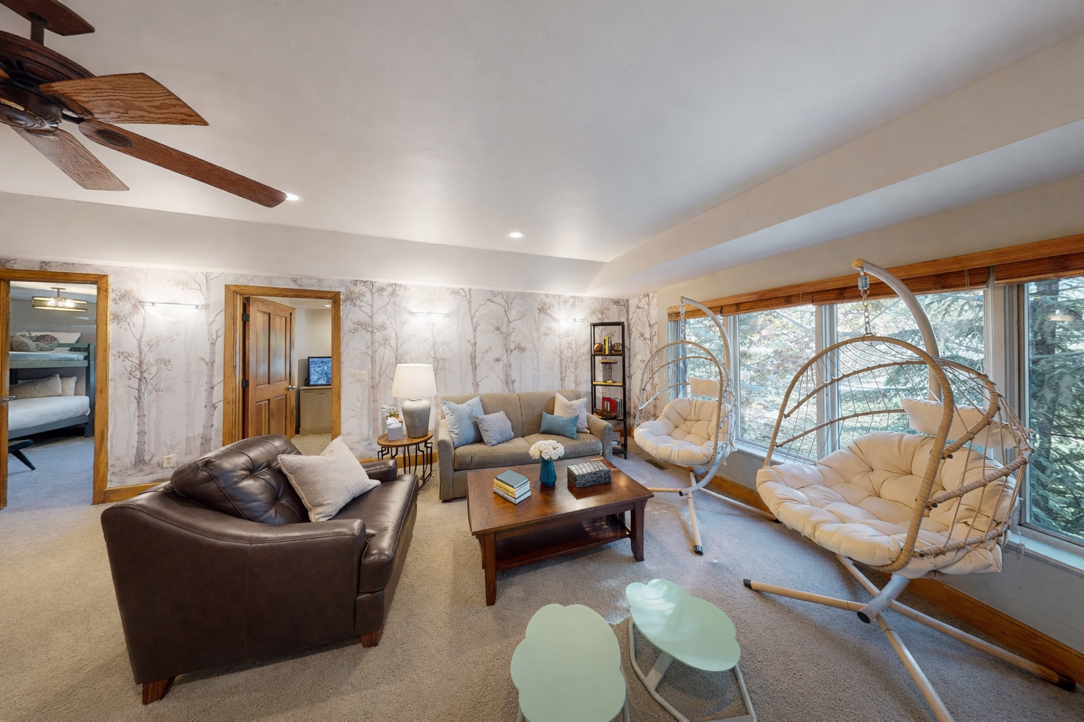 Unwind in your stylish living room with a unique hanging chair, cozy seating, and peaceful forest views through large windows.