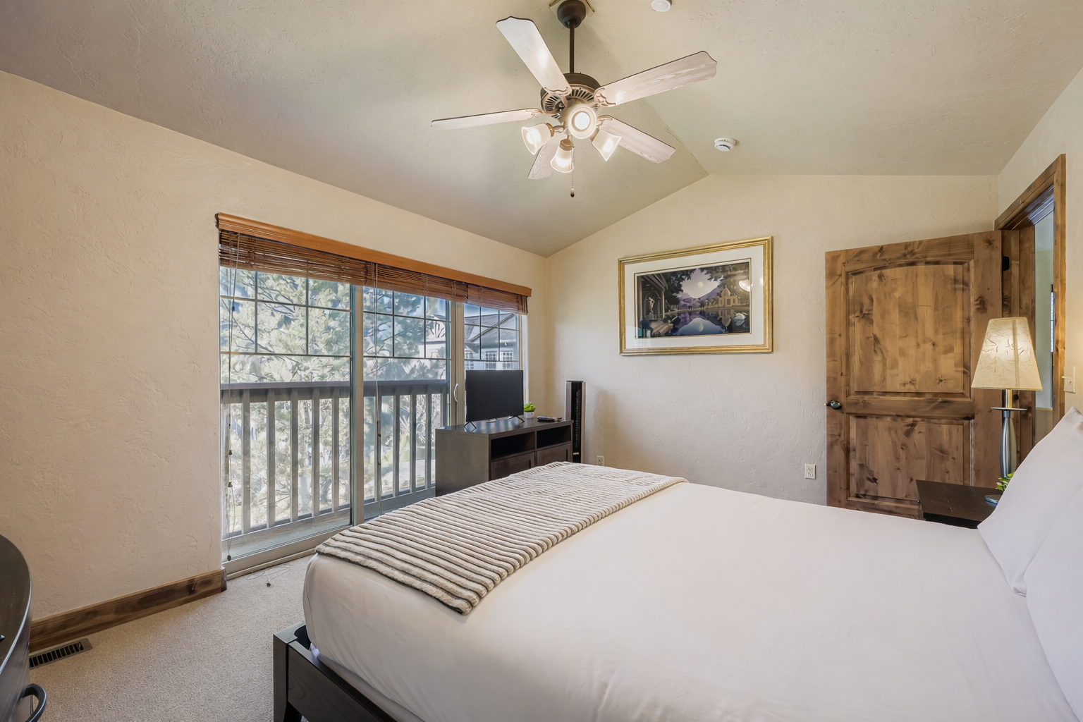 Relax in your spacious bedroom featuring a comfortable bed, entertainment center, and private access to outdoor views through sliding glass doors.
