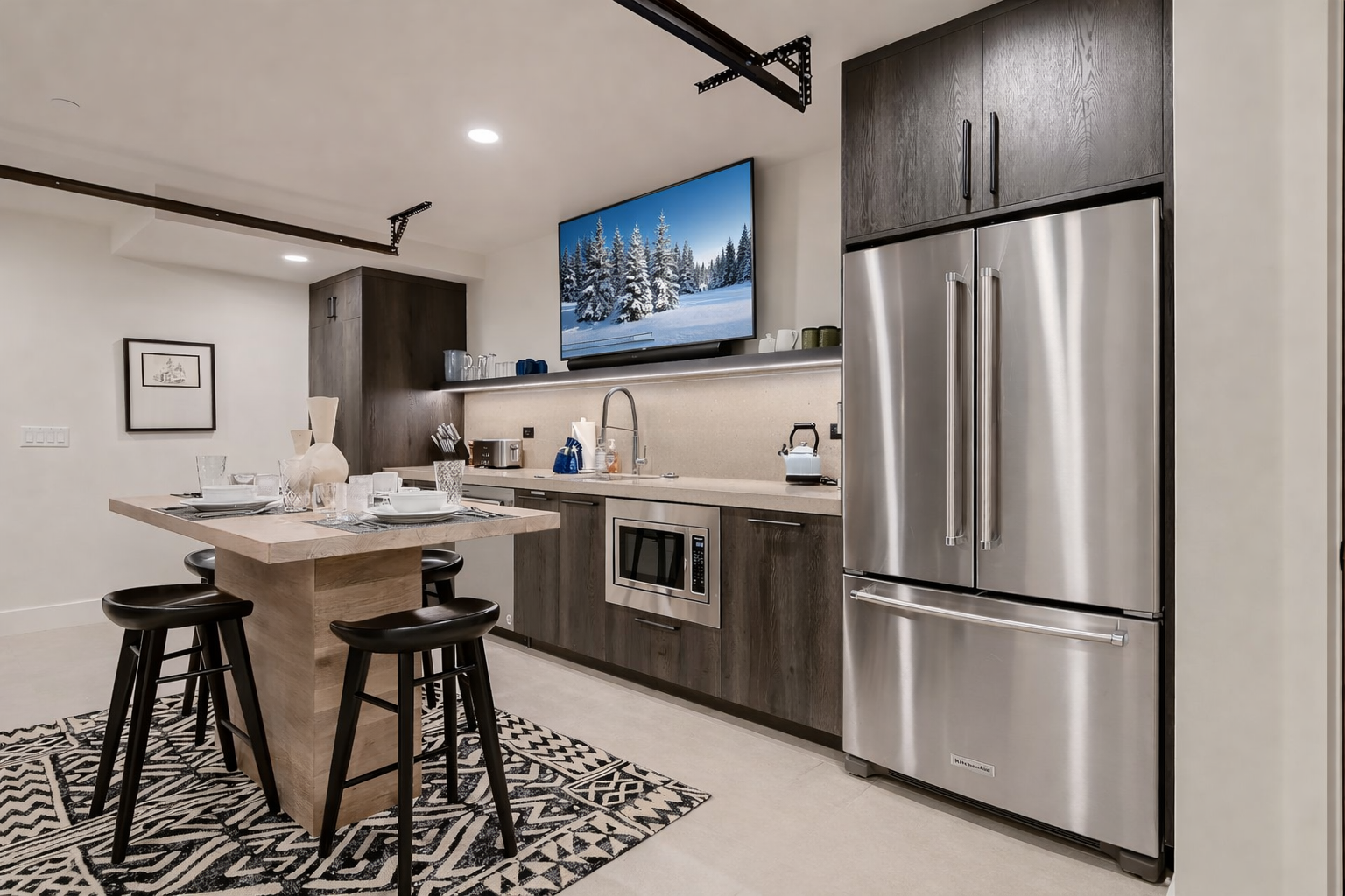 Whip up a meal or snack in this fully-equipped mother-in-law modern kitchen, featuring stainless steel appliances, a large island with seating, and even a TV for entertainment.