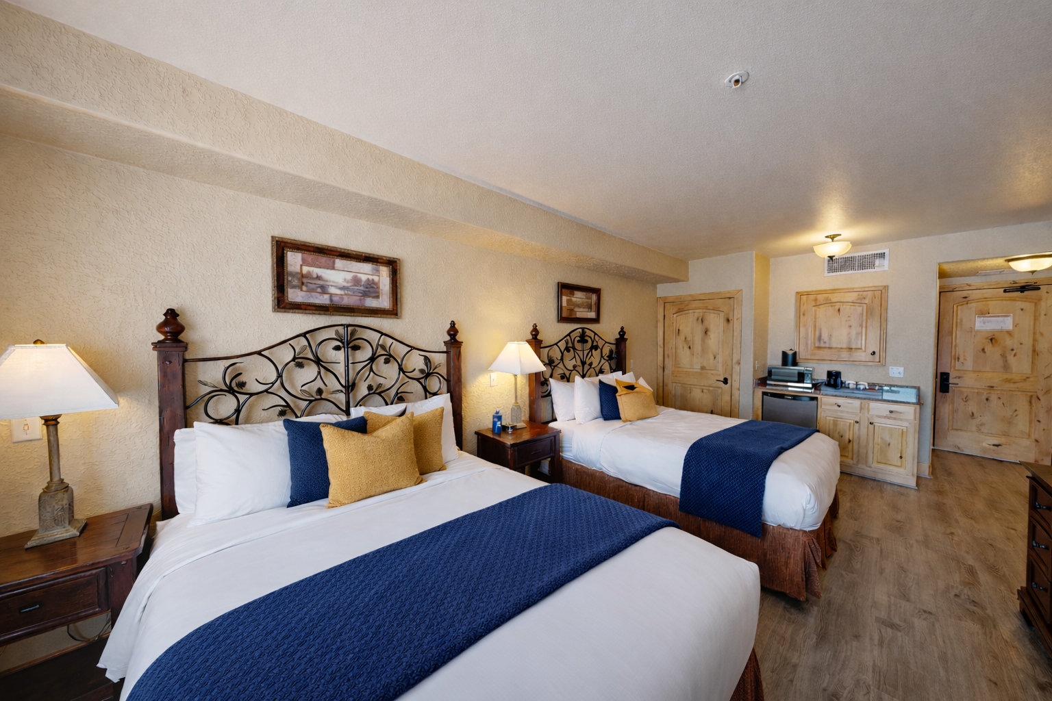 This spacious guest room features two plush queen beds with ornate wrought-iron headboards. Enjoy the convenience of a private kitchenette and sleek wood flooring, perfect for a group getaway.