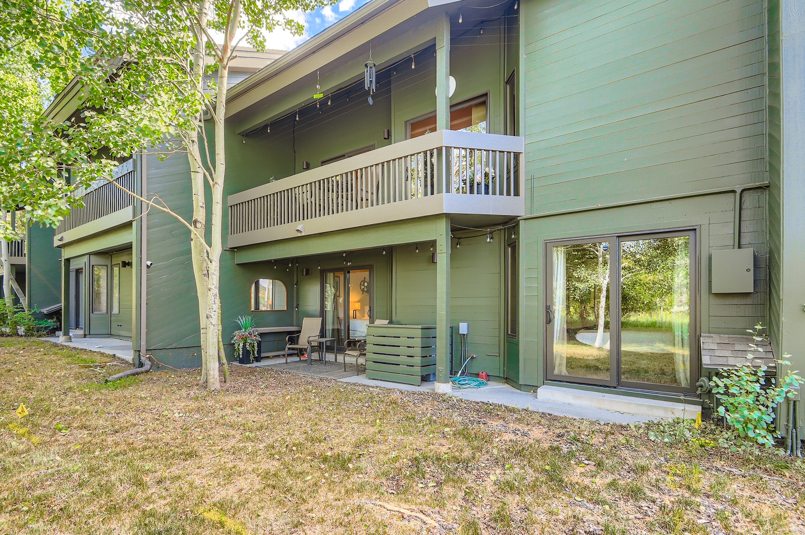 A two-story vacation rental nestled among trees, featuring private balconies, ground-level patio seating, and natural surroundings perfect for a peaceful mountain getaway.