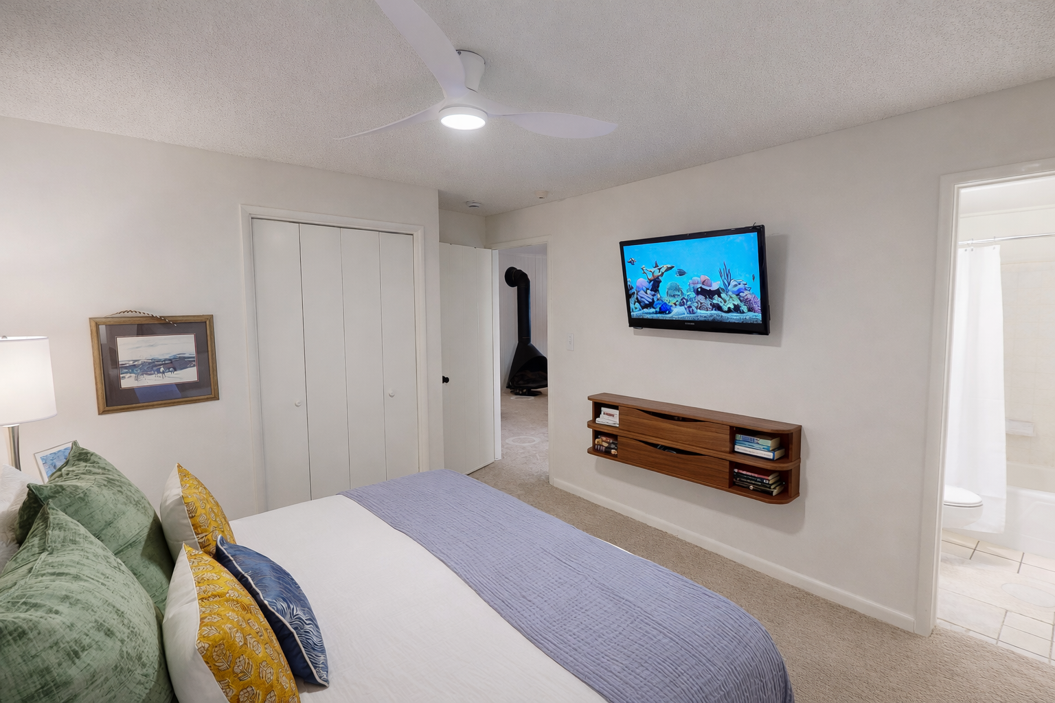 Unwind in your modern bedroom featuring a wall-mounted TV, cozy bedding, and floating entertainment console for relaxing evenings.