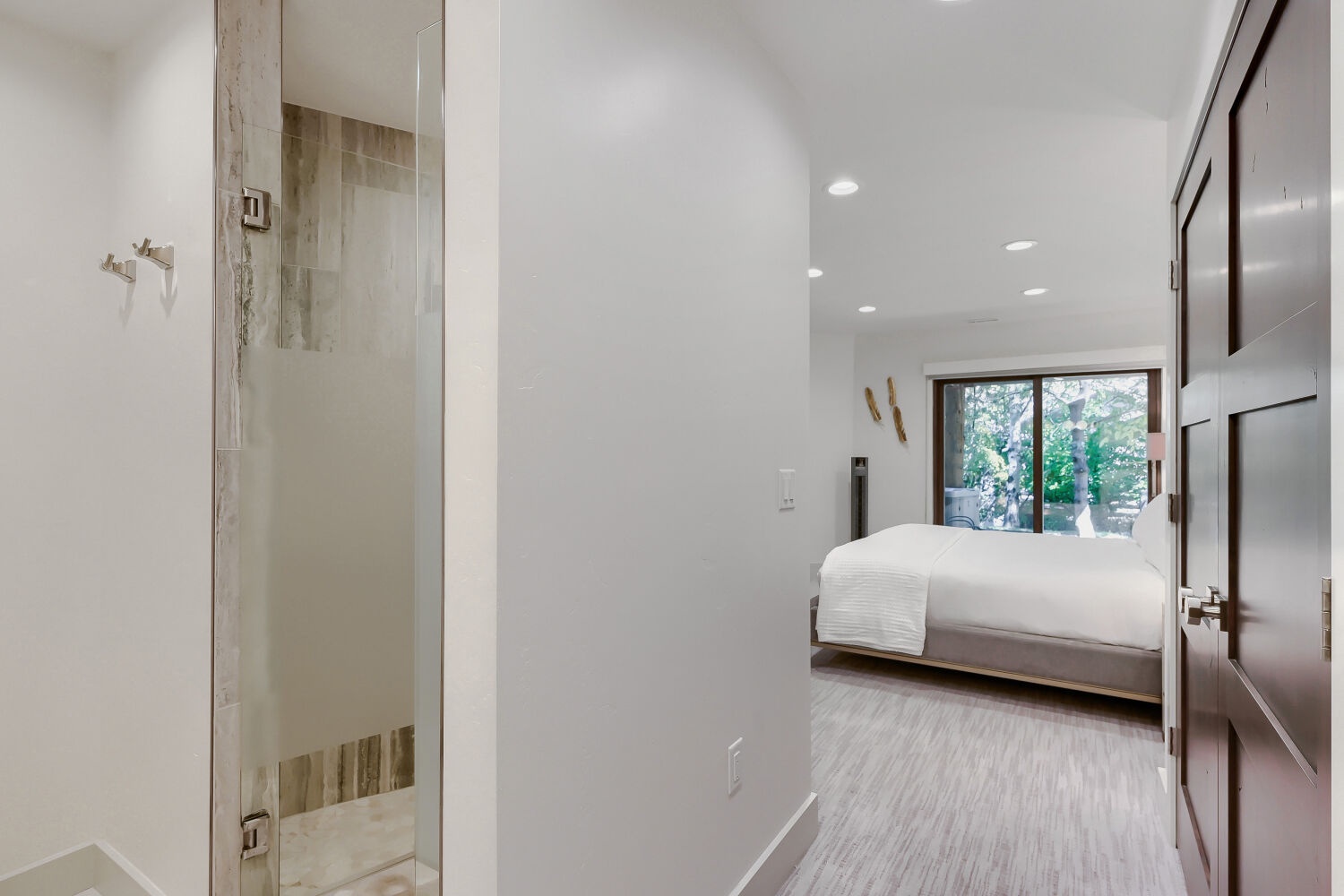 Step into your serene retreat, where a bright bedroom with garden views opens to a beautifully appointed bathroom with a glass-enclosed shower waiting for your arrival.