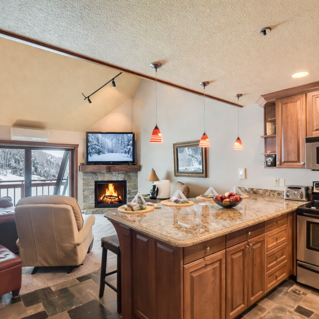 Cozy open-concept kitchen and living area with granite counters, warm wood cabinetry, a stone fireplace, and mountain views. Perfect for cooking, relaxing, and enjoying après-ski comfort during your Park City stay.