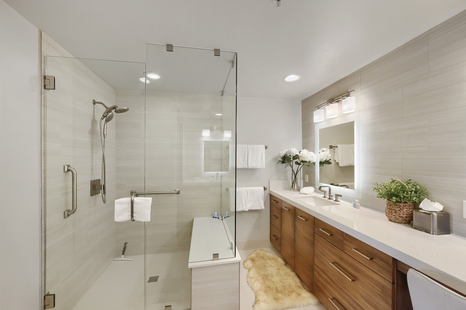 Step into your spa-inspired bathroom with sleek glass shower, warm wood vanity, and fresh white linens awaiting your arrival.