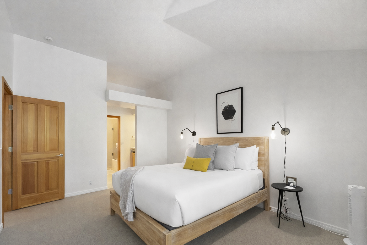 Discover tranquility in this bright, minimalist bedroom featuring a comfortable natural wood bed and a cozy daybed. Large windows offer serene views of the outdoors.