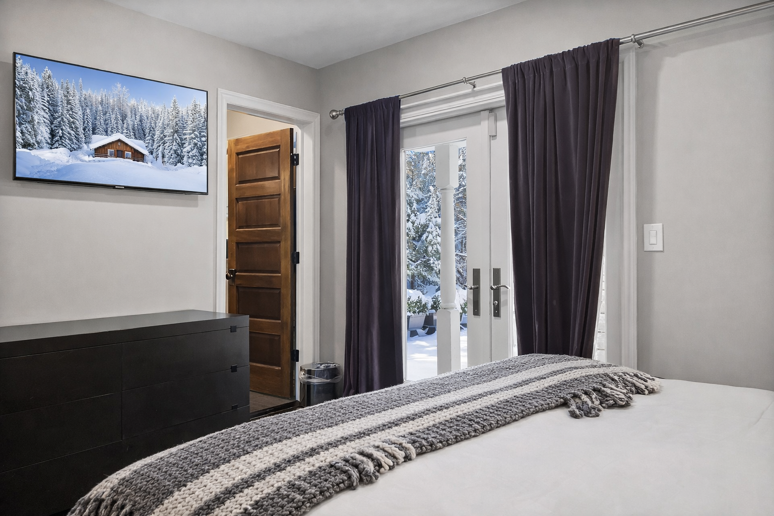 Your cozy bedroom opens to snowy mountain views through elegant French doors, creating the perfect winter retreat.