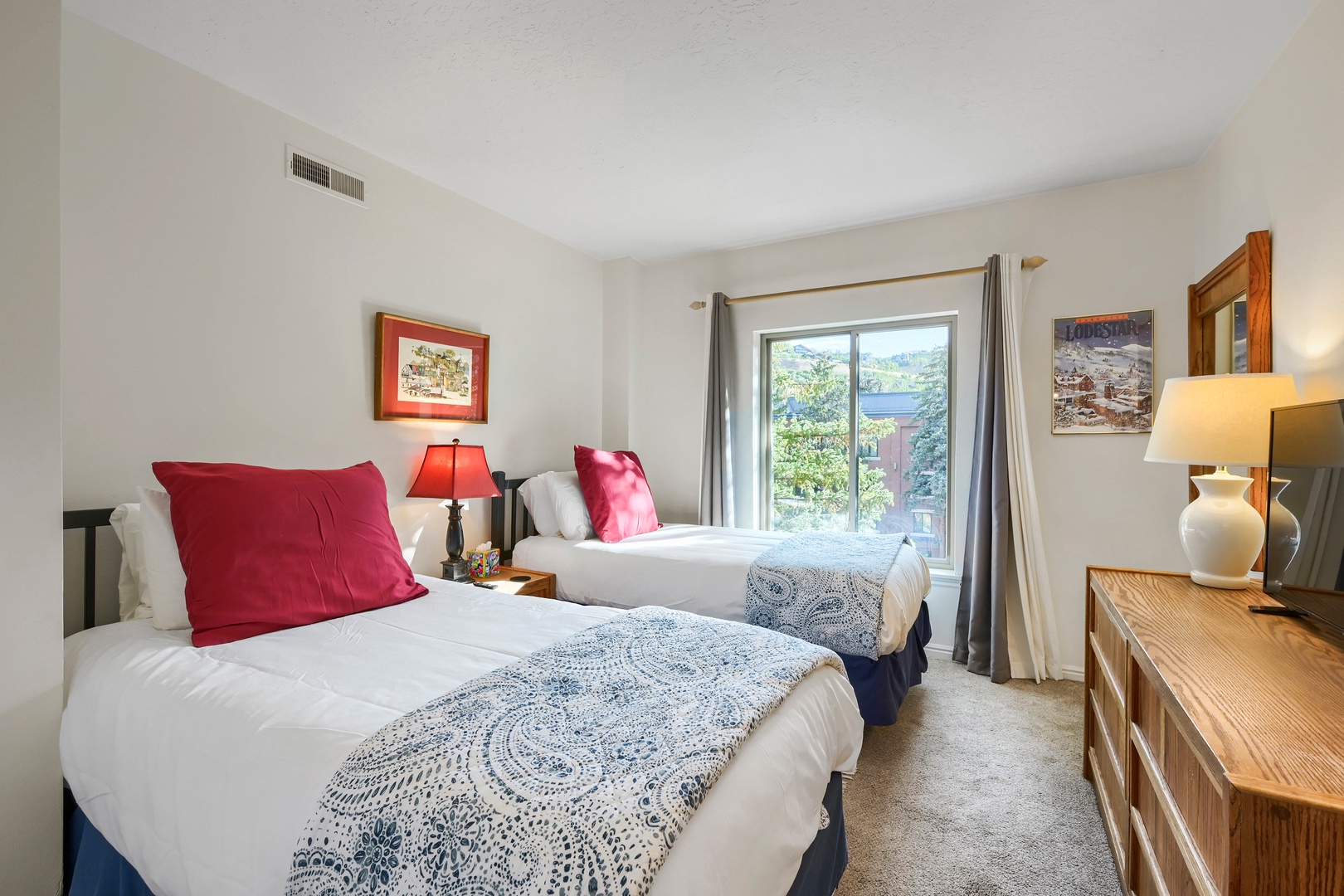 Two cozy beds await your arrival, each with plush linens and cheerful accent pillows. Natural light streams through your window, framing peaceful neighborhood views for a restful stay.