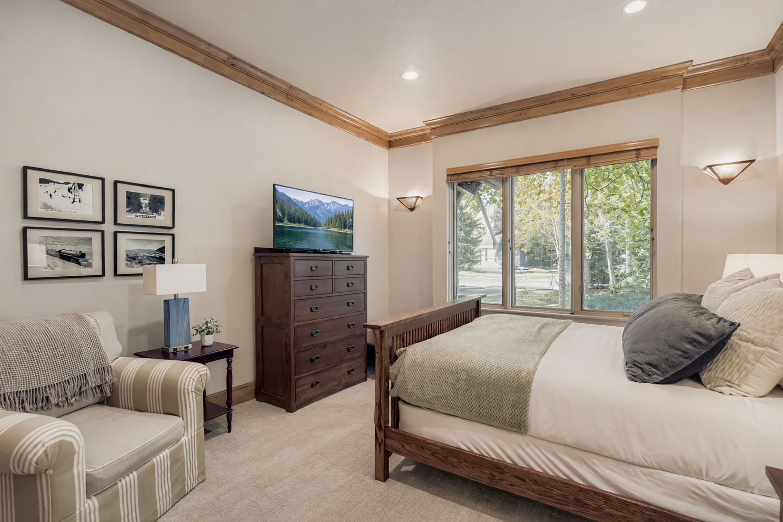 Unwind in the tranquil main floor queen bedroom. Features a plush bed, dark wood furnishings, light wood floors, and large windows with serene forest views for a peaceful stay.