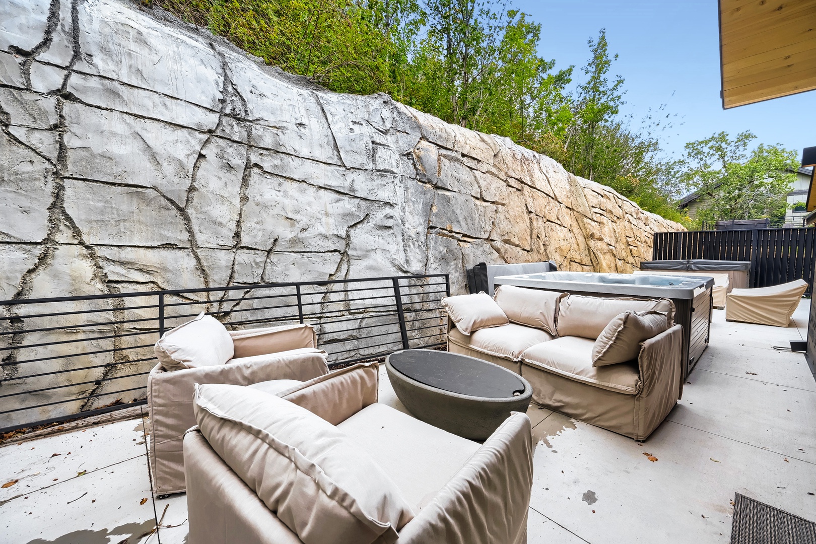 Outdoor lounge area with plush seating, a fire pit, and hot tub set against natural rock—perfect for unwinding under the open sky.