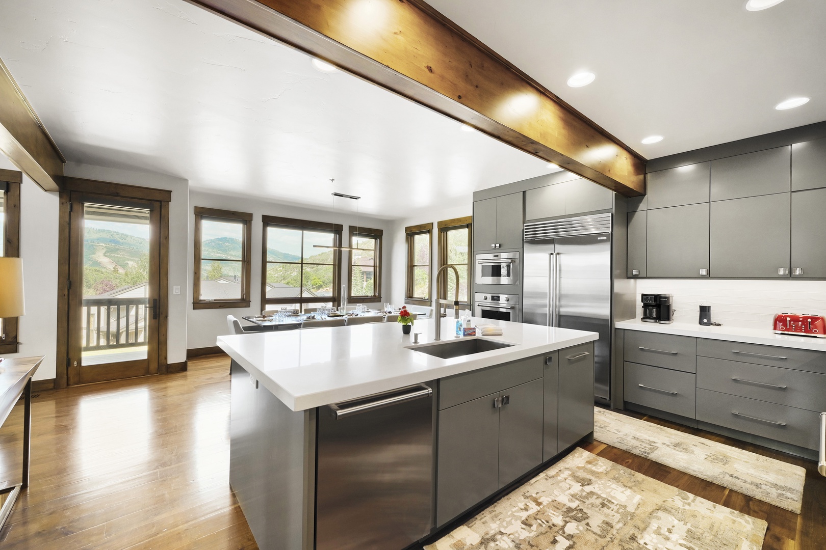A sleek modern kitchen awaits your culinary adventures, featuring a spacious island, stainless steel appliances, and mountain views through expansive windows framed by warm wood accents.