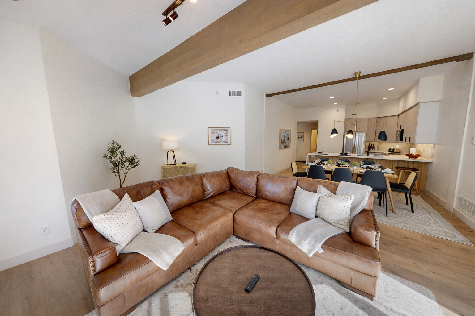 Sink into the warm leather sofa and feel the sunlight streaming through floor-to-ceiling windows as exposed beams create cozy charm above.
