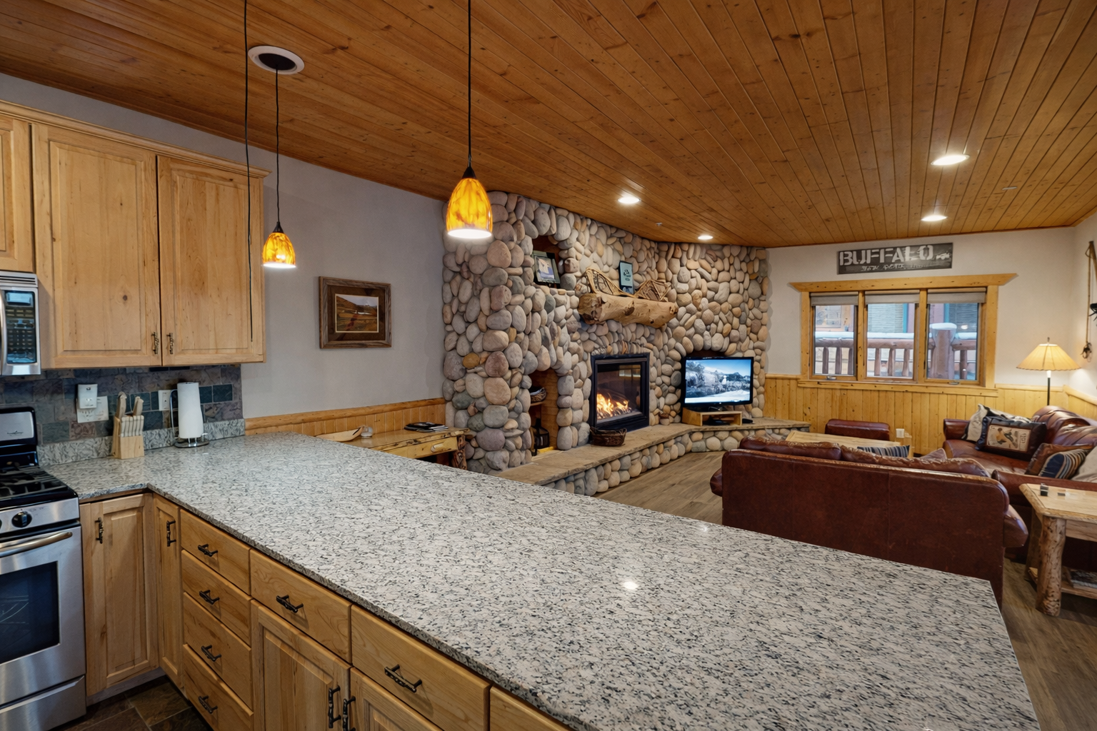 Your open kitchen flows into a cozy living space where granite counters meet rustic stone fireplace warmth.