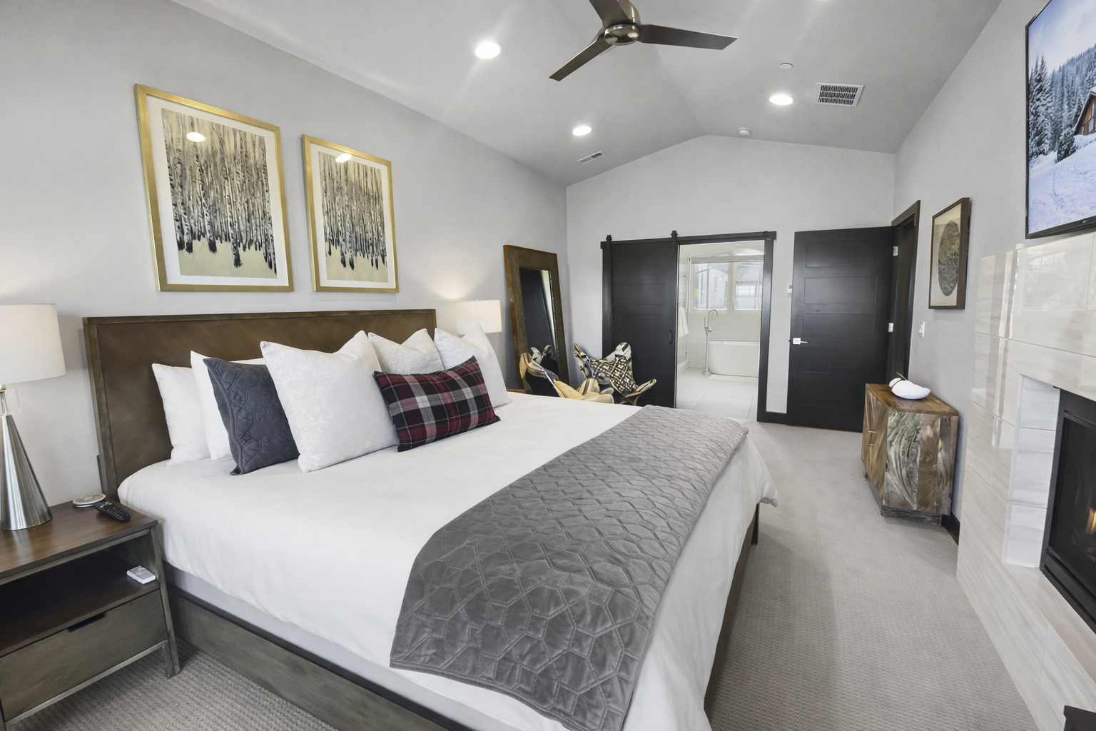 This vaulted primary suite features a king-size bed, private fireplace, and dedicated workspace. Large glass doors open to a scenic balcony, creating a sun-filled, luxurious mountain retreat.